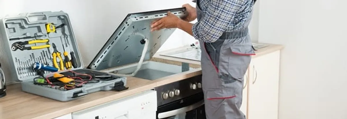 Cooktop repair technician lifting a built-in stovetop for service in Atlanta, GA